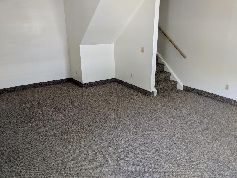 a carpeted room with stairs and a white wall