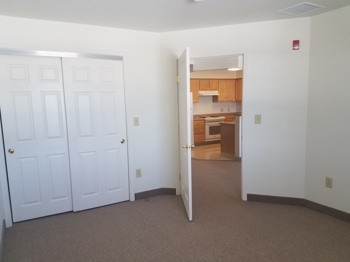 an empty room with two doors and a kitchen in the background