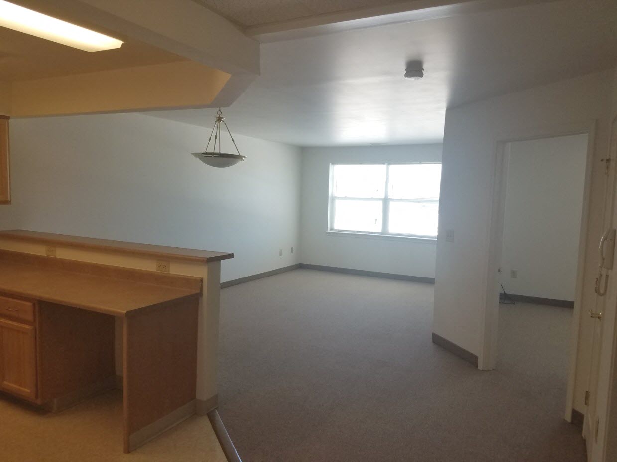 an empty living room with a desk and a window