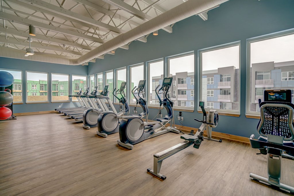 a gym with cardio equipment and windows