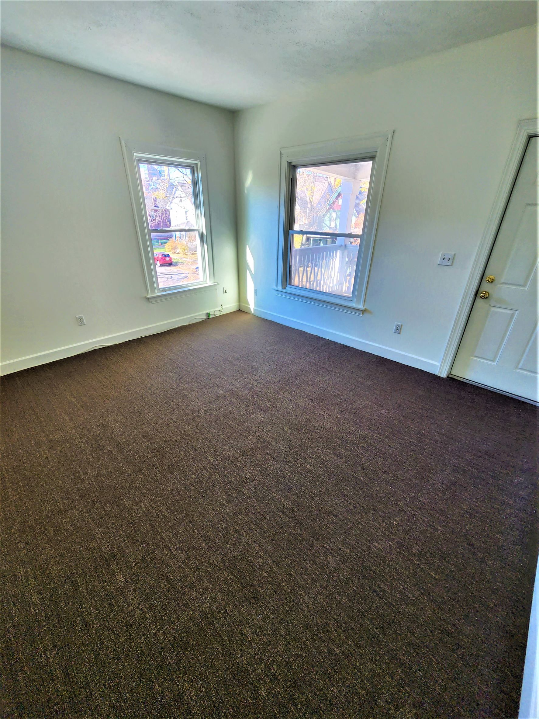 a carpeted room with two windows and a door