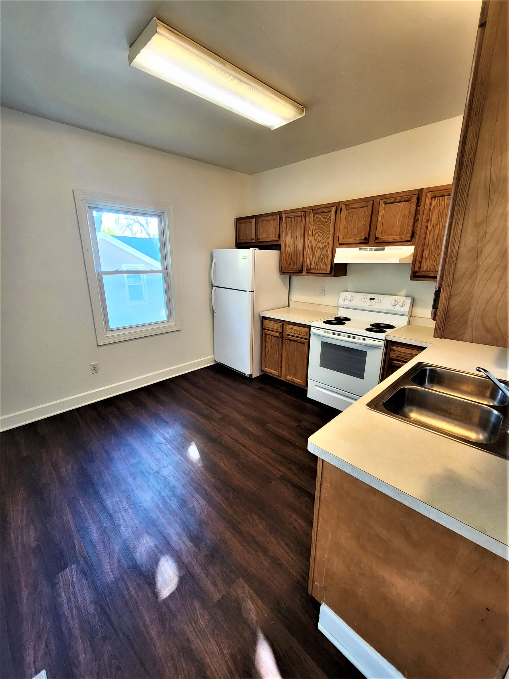 an empty kitchen with wooden floors and white appliances