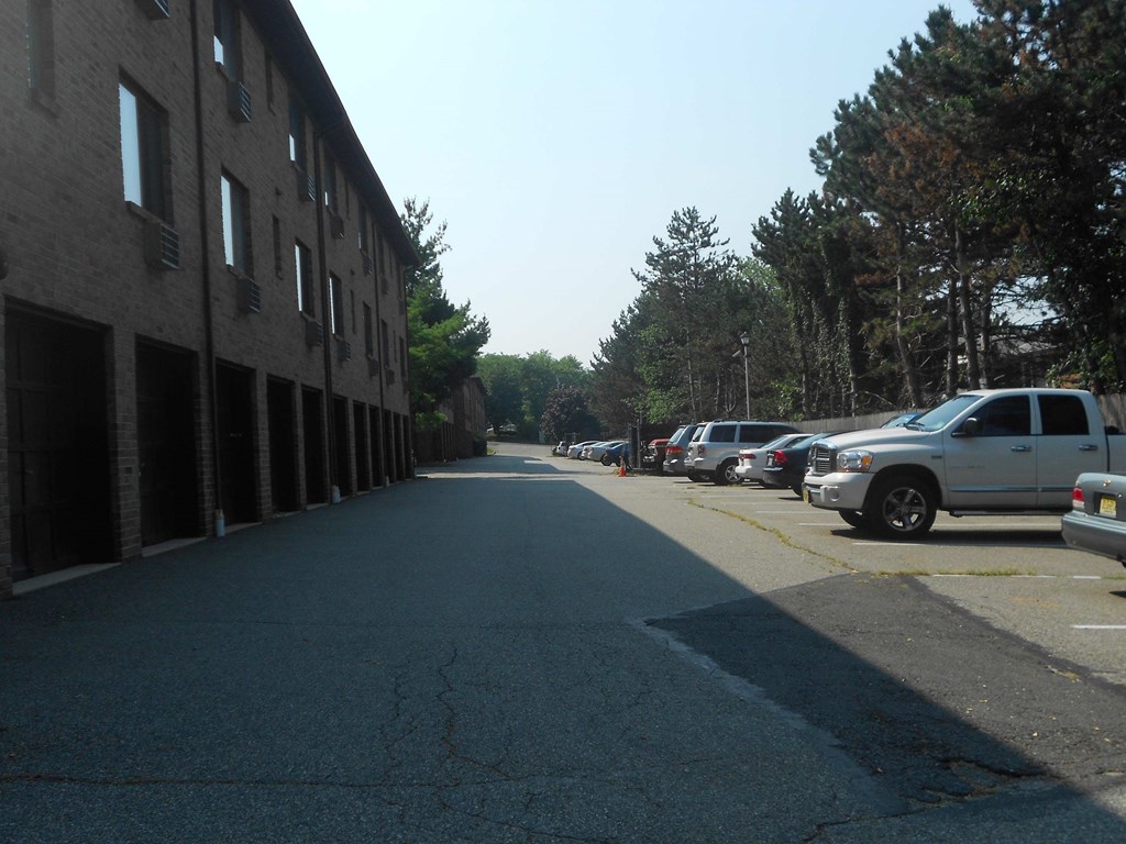 A long, empty street with cars parked on the side and a building on the left.