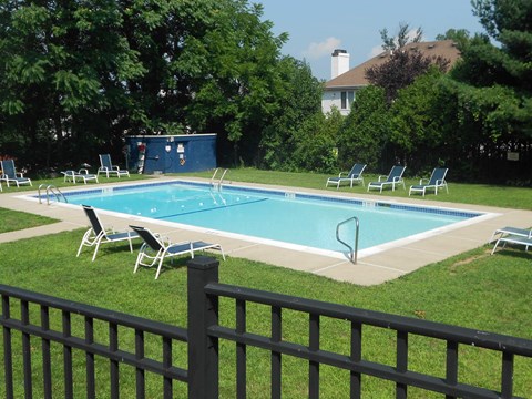 A pool surrounded by lawn chairs and a fence.
