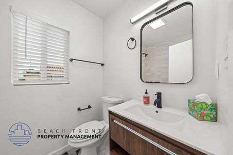 A bathroom with a toilet, sink, mirror, and a window with blinds.