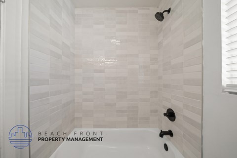 A white tiled shower with a black faucet and a logo for Beach Front Property Management.