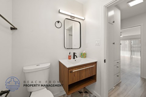A bathroom with a white toilet, a sink with a mirror above it, and a wooden cabinet below the sink.