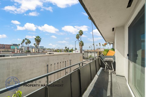 A balcony with a table and chairs overlooks a cityscape with palm trees.