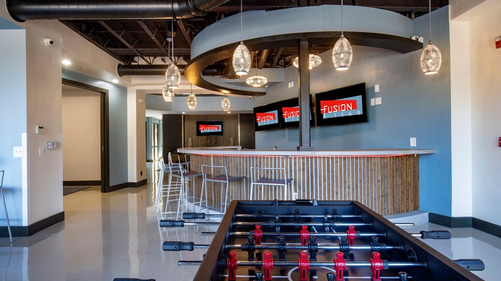 A foosball table is in the middle of a room with a bar in the background.