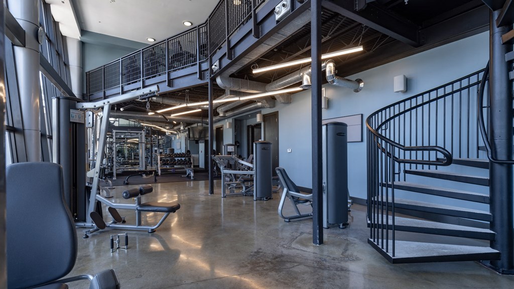 A gym with a spiral staircase and a variety of equipment.