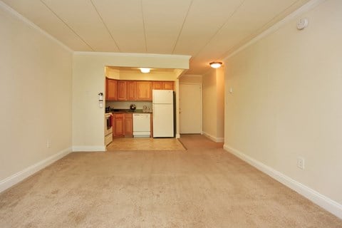 the spacious living room and kitchen with white appliances and beige carpeting