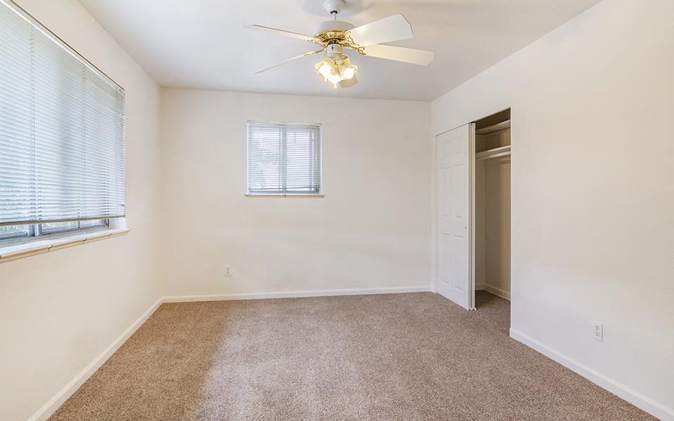 an empty bedroom with a ceiling fan and a window
