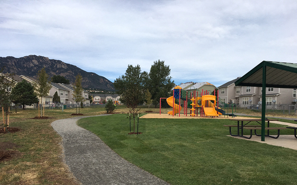 a playground in a park with houses and mountains in the background
