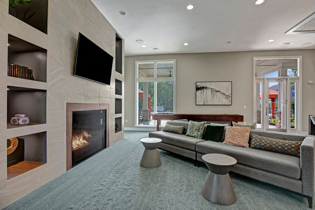 Living room at Ascent at Mallard Creek Apartment Homes. Carpet area with a fire place, tv, couch, pool table, tables, and big windows.
