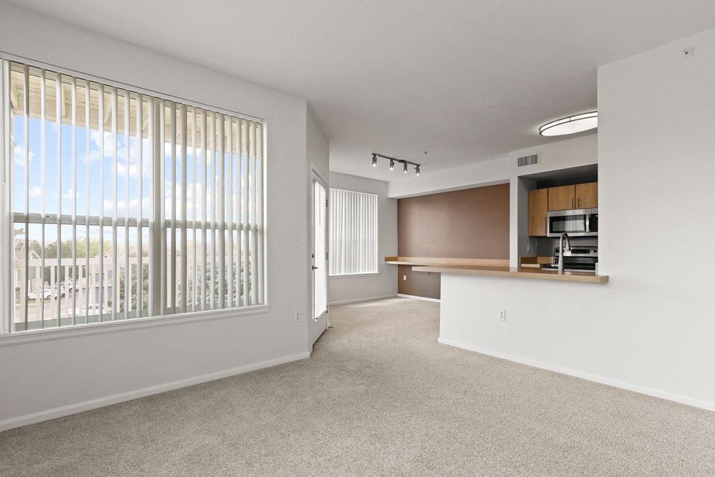an empty living room with a large window and a kitchen