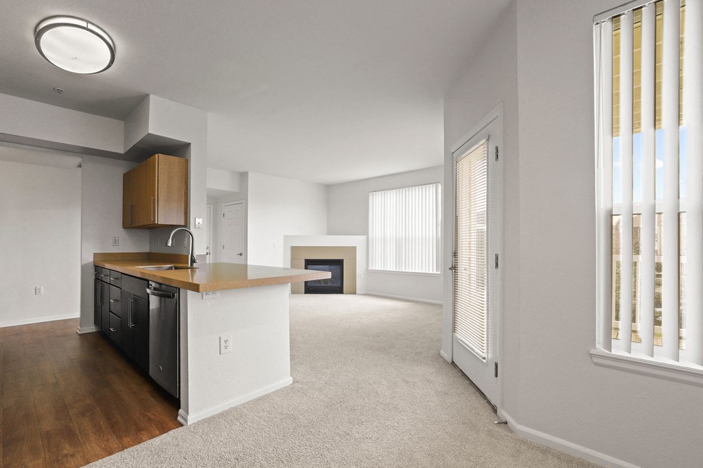 an empty living room with a kitchen and a fireplace