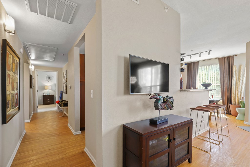 a living room with a tv on the wall and a dining room with stools
