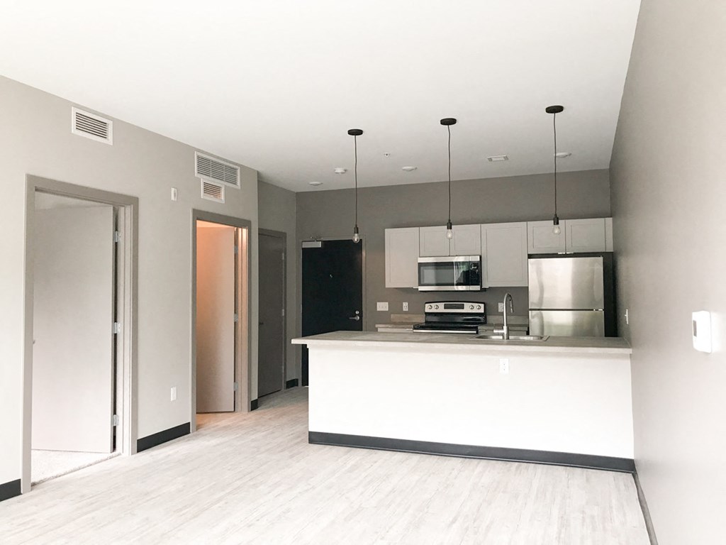 an empty living room with a kitchen and a door to a hallway