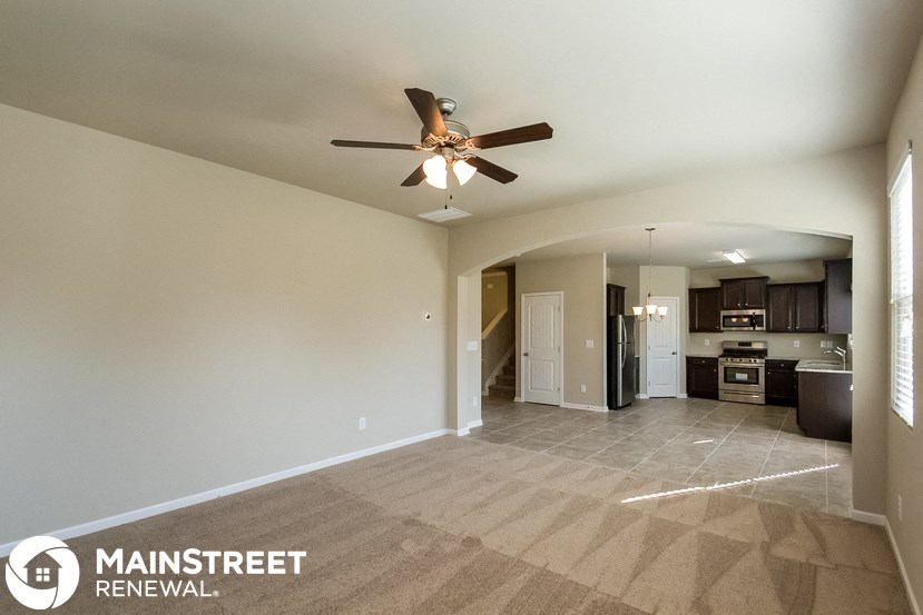 an empty living room with a ceiling fan and a kitchen