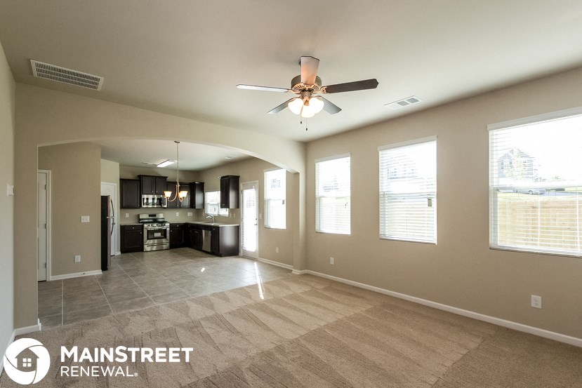 an empty living room with a ceiling fan and a kitchen