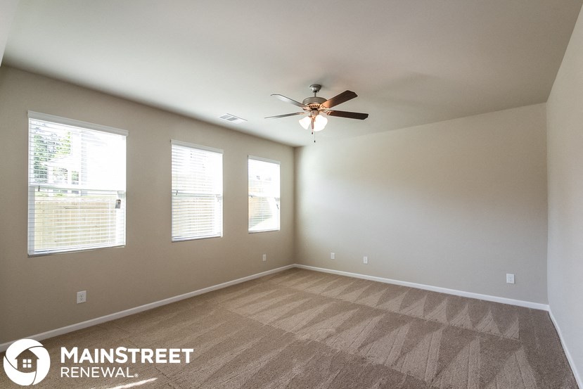 an empty room with a ceiling fan and three windows