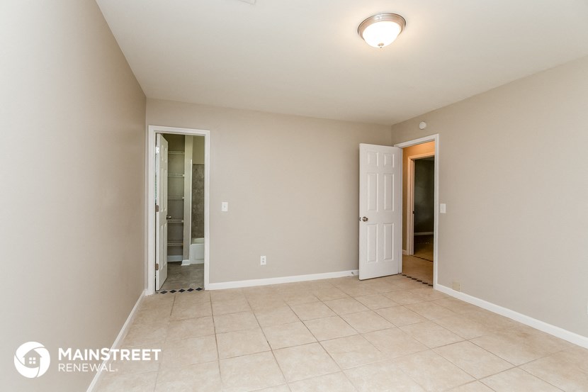 a spacious living room with tile flooring and a door to the bathroom