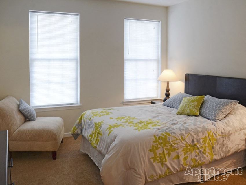 a bedroom with a bed and a chair and two windows