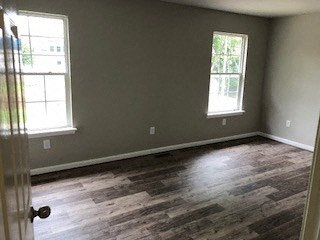 an empty room with wood floors and two windows