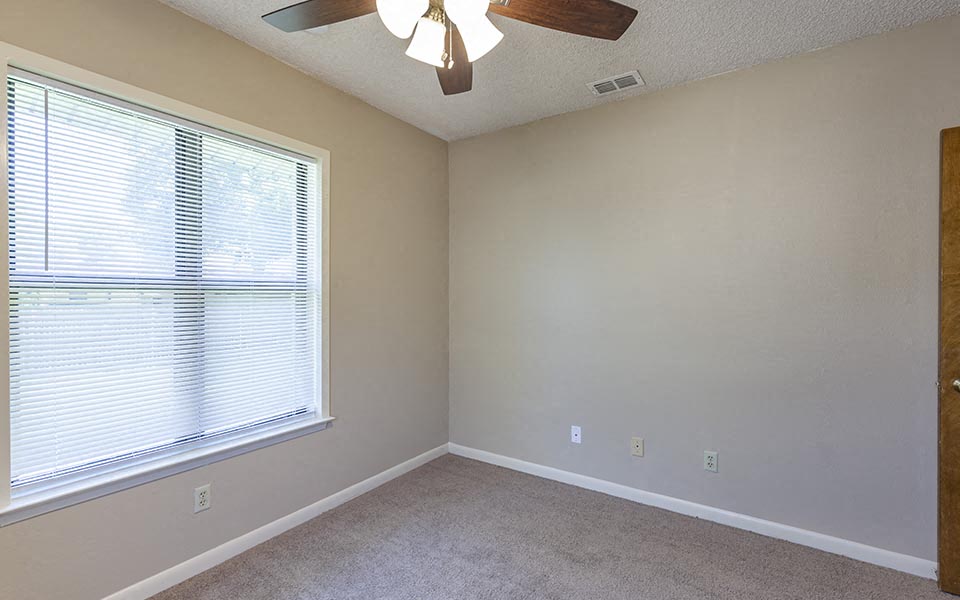 an empty bedroom with a large window and a ceiling fan