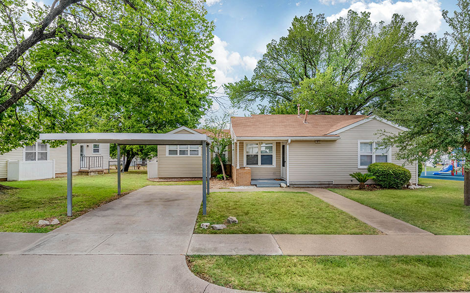 a small white house with a driveway and trees