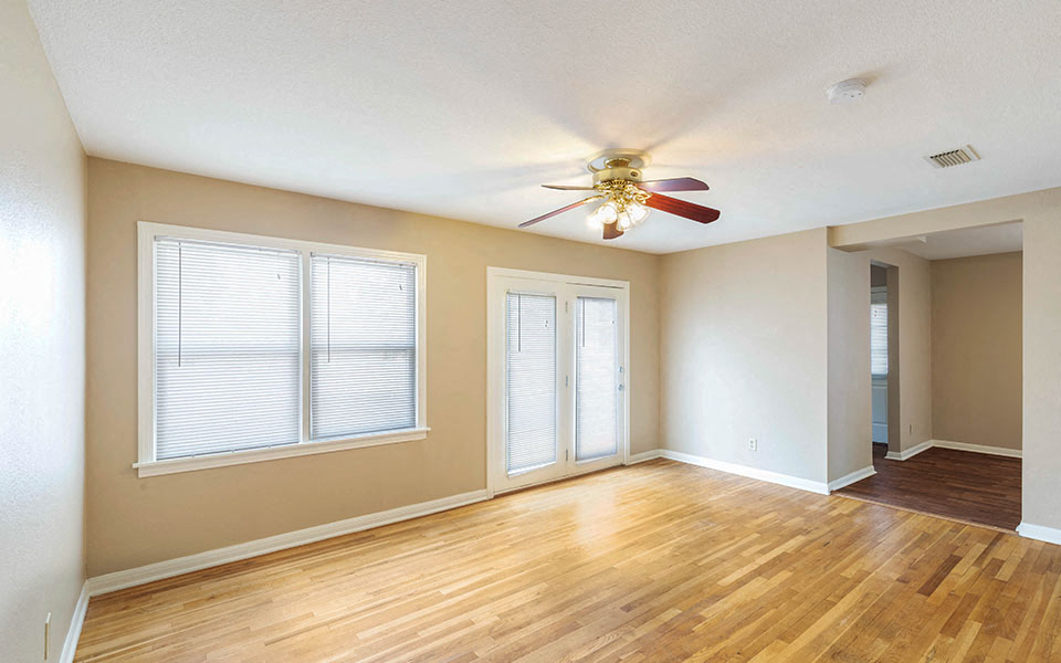 an empty living room with a ceiling fan and window