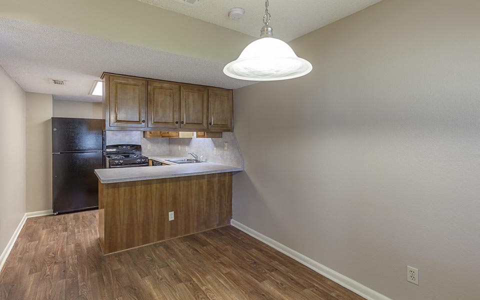 an empty kitchen with wood floors and a black refrigerator