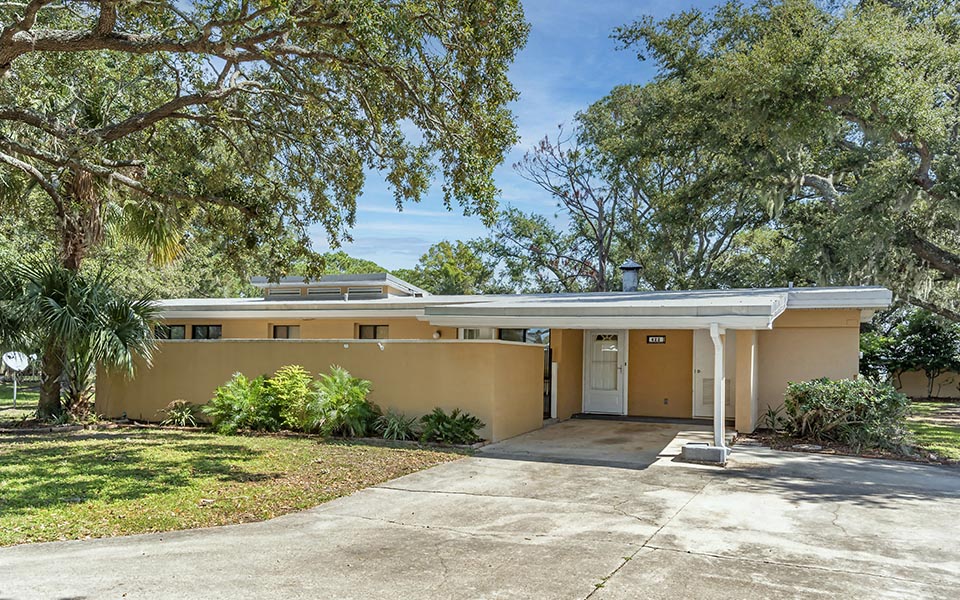 a yellow house with a driveway and trees