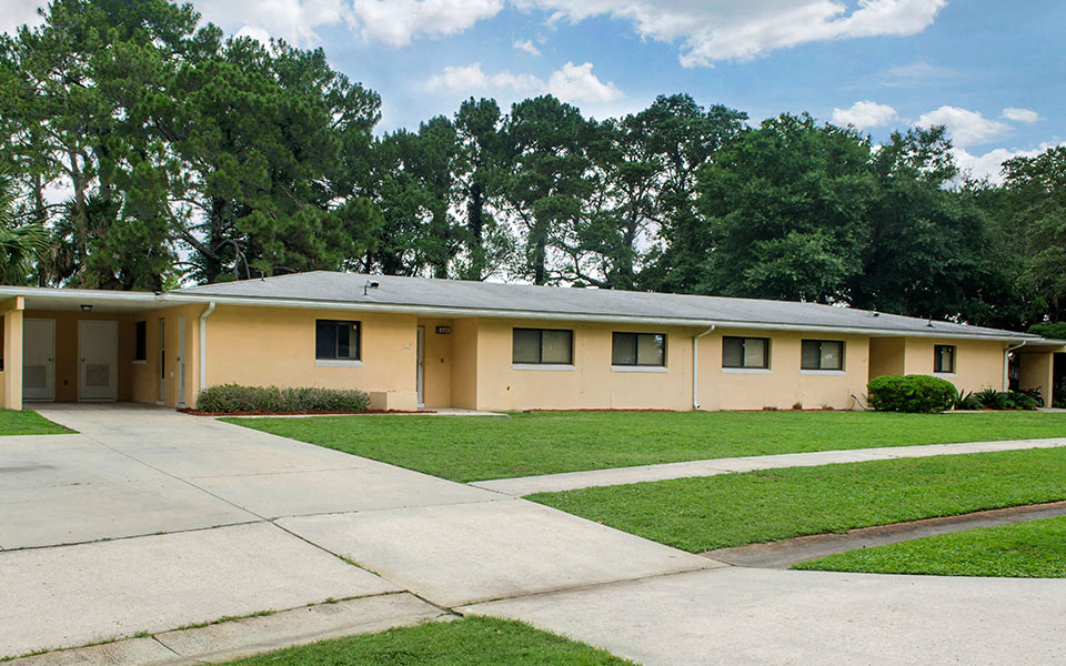 the front of a yellow house with a driveway and grass
