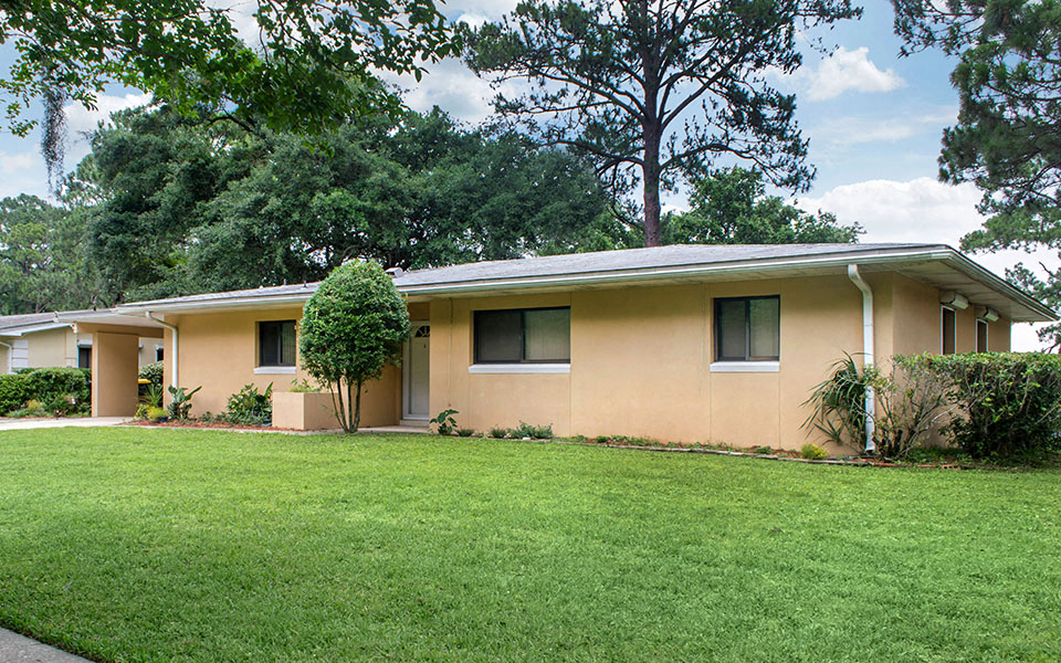 a yellow house with a green lawn and trees