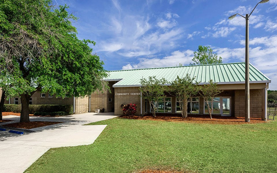 the front of a brick building with a green roof and trees