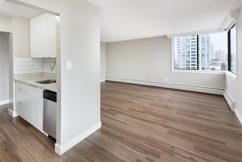 an empty living room and kitchen with wood flooring and a window