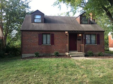 A small red brick house with a brown door and a small porch.