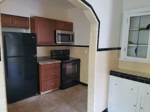 A black refrigerator is in a kitchen with brown cabinets and a black microwave.