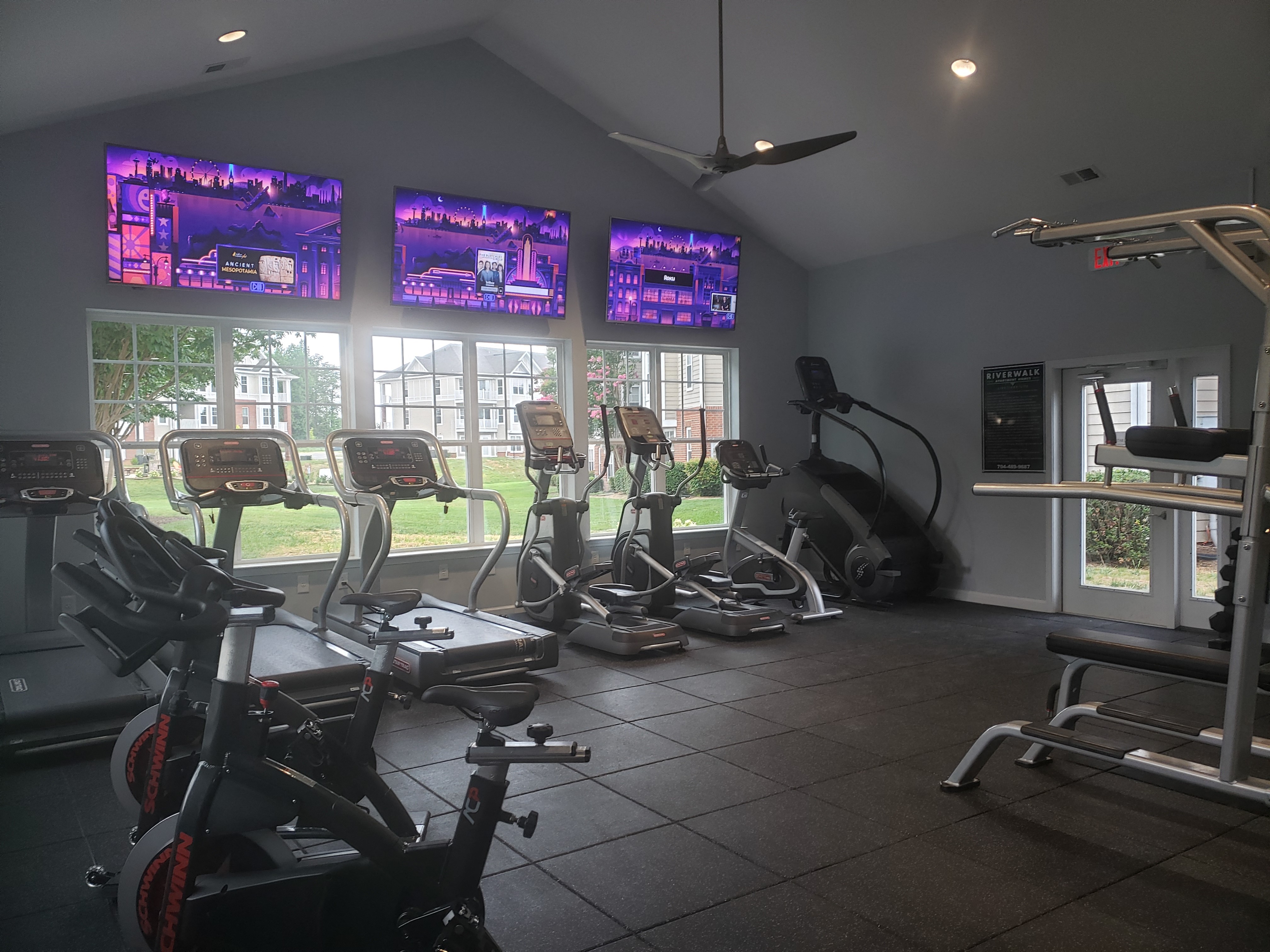 a gym with various exercise machines and three televisions