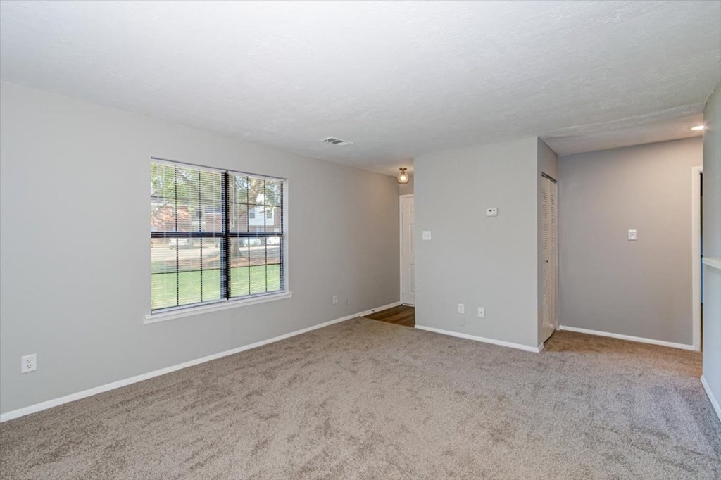 a spacious living room with a large window and carpeting