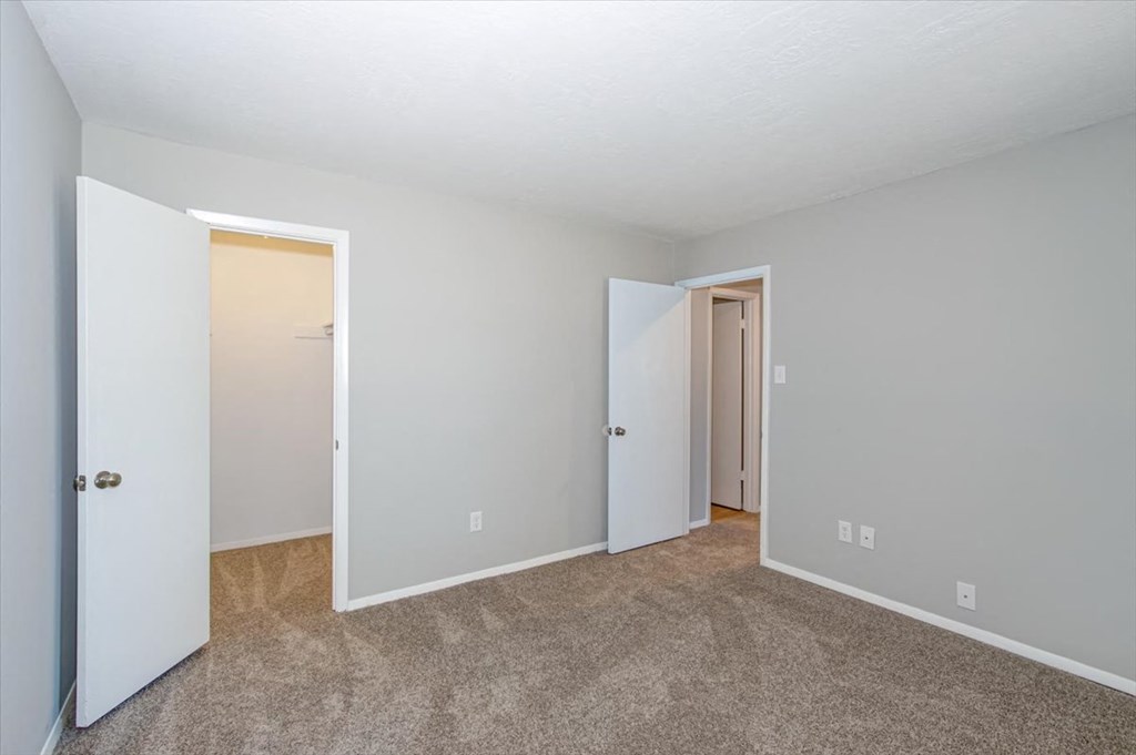 a bedroom with white walls and carpeting and a door to a closet