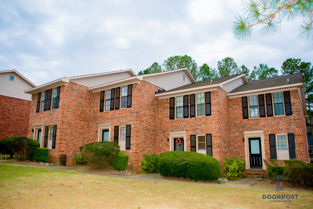 the front of a brick house with green grass and trees
