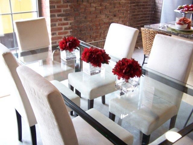a glass table with white chairs and red flowers on it