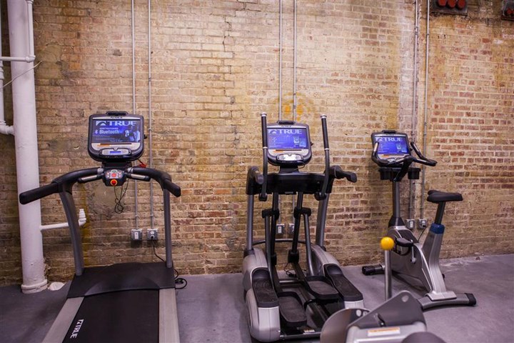three exercise machines in a gym with a brick wall