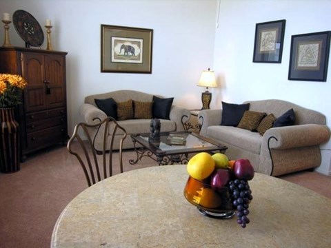 A living room with a couch, chairs, a coffee table, and a vase of fruit on the table.