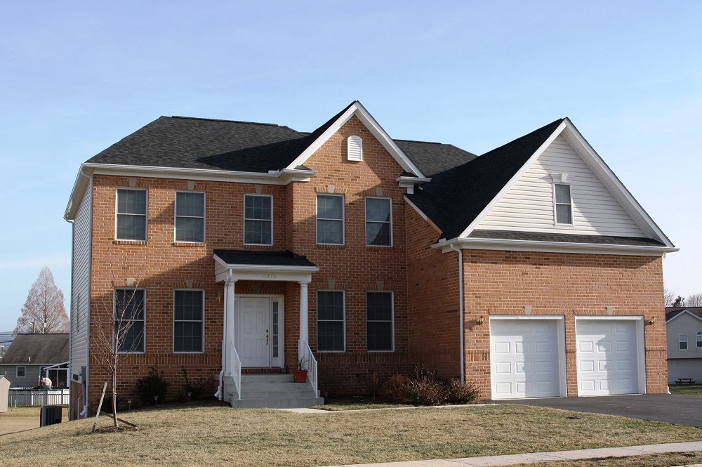 a brick house with white garage doors and a black roof