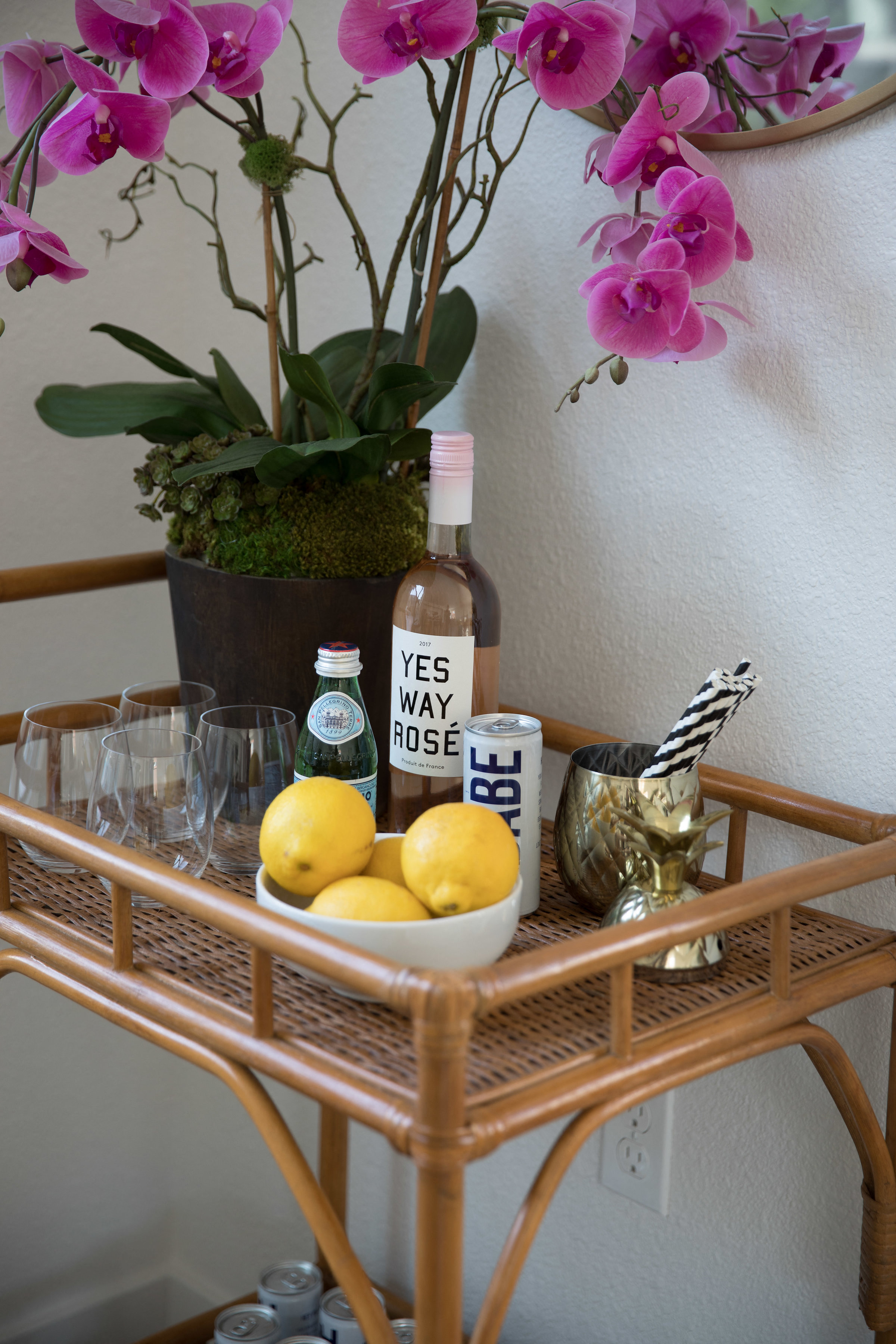 a table with a bowl of lemons and a bottle of wine and some flowers