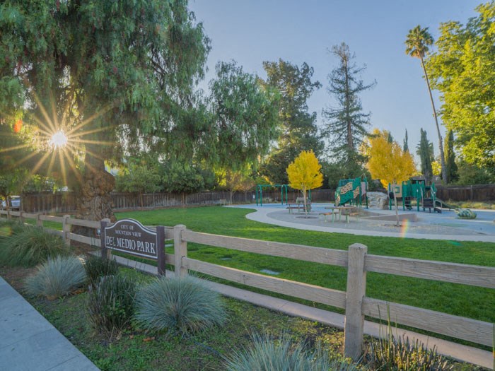 a park with a playground and the sun shining through the trees