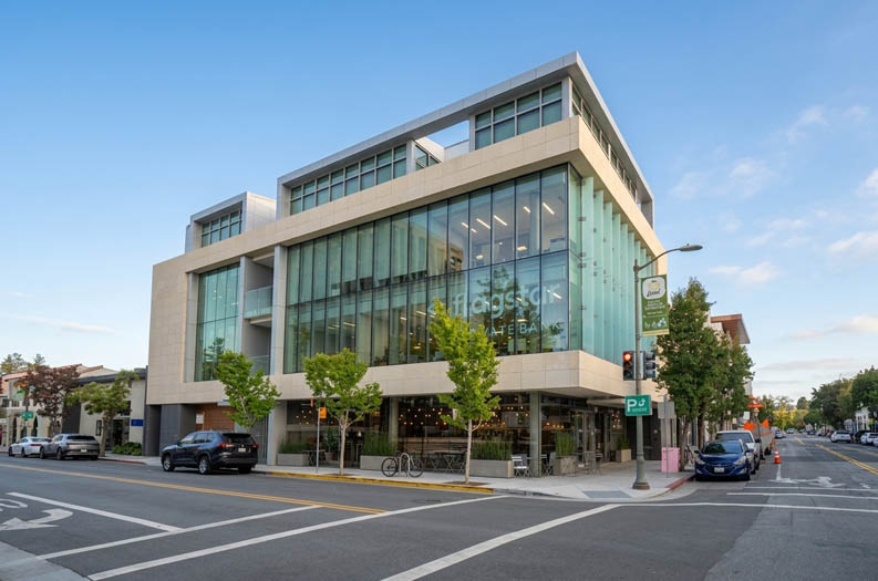 A modern building with glass windows and a sign that reads "magso" is situated on a street corner with cars parked in front.